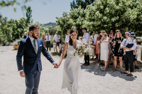 Händchen haltendes Brautpaar inmitten der Hochzeitgesellschaft