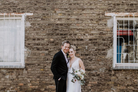 Fotoaufnahme des Hochzeitspaares vor einer Backsteinmauer