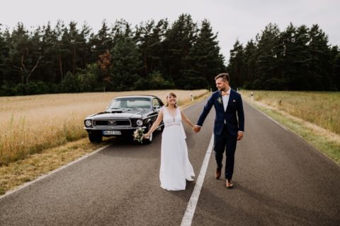 Brautpaar Spaziergang mit Mustang im Hintergrund